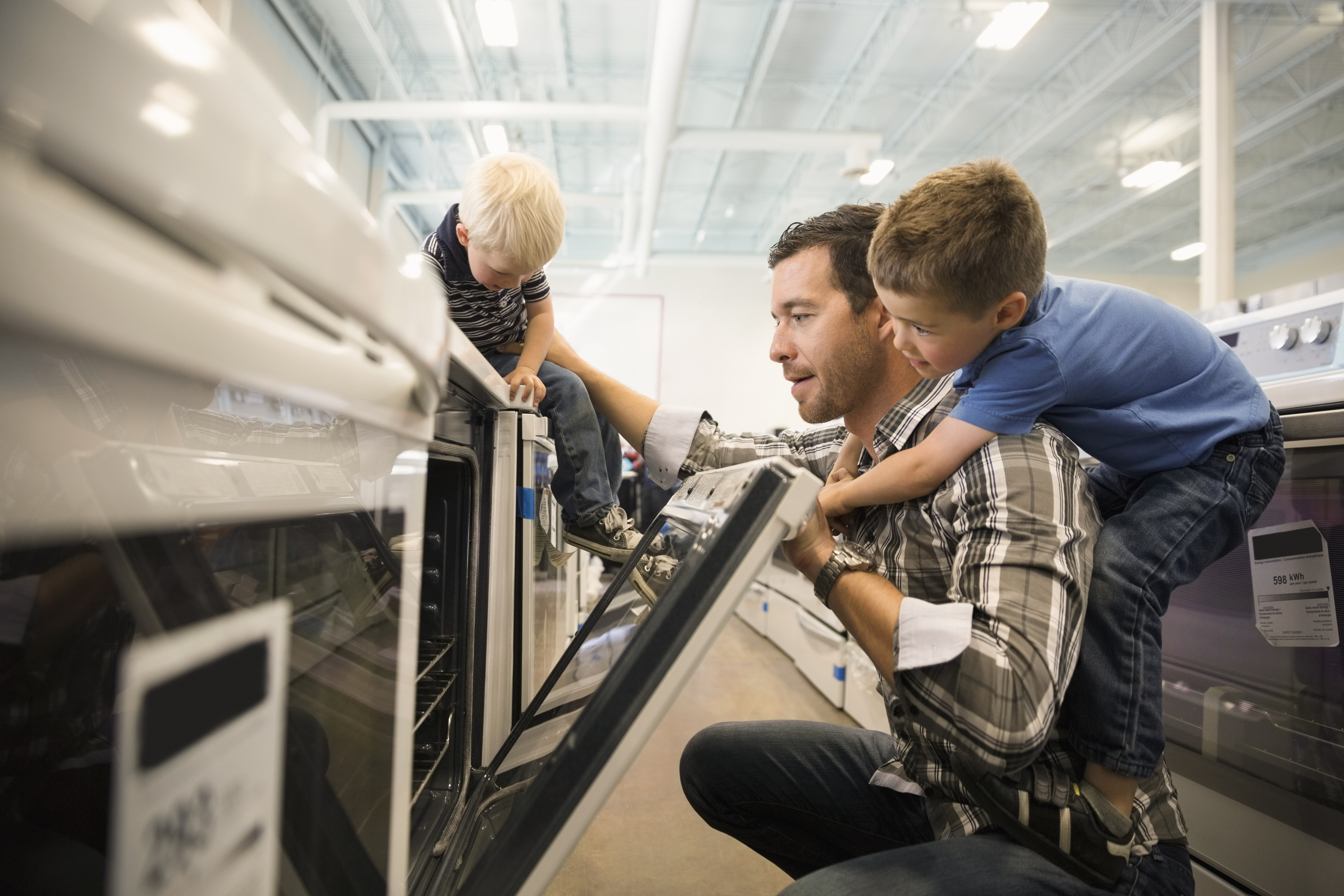 Man med två barn är i en butik och tittar på ugnar