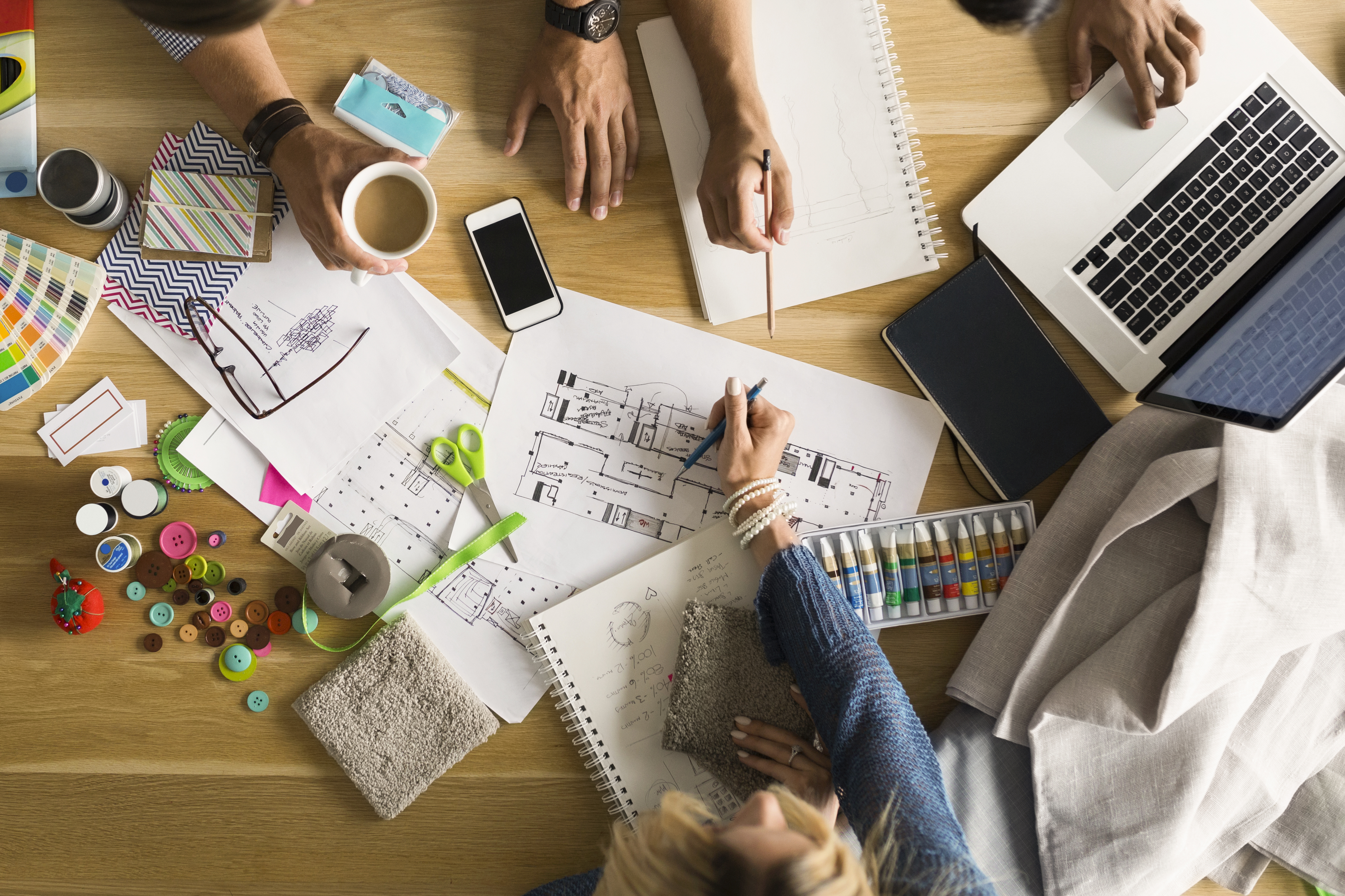 Bord med knappar, färgprover, teckningar och händer som håller i pennor